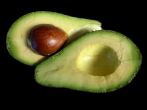 avocado cut in half with brown seed showing green and yellow inside black background Pantothenic Acid Vitamin B5 nutrients from plants