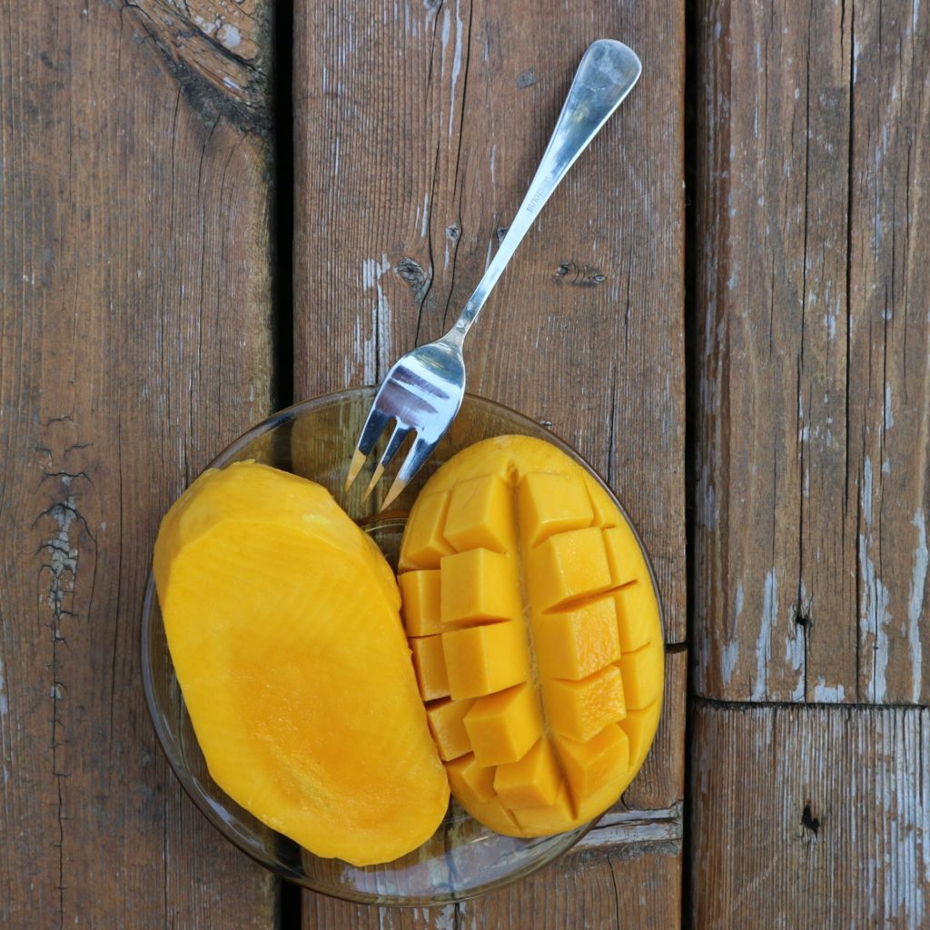 cut mango on a clear plate with a silver fork on top of wood table - foods I avoid